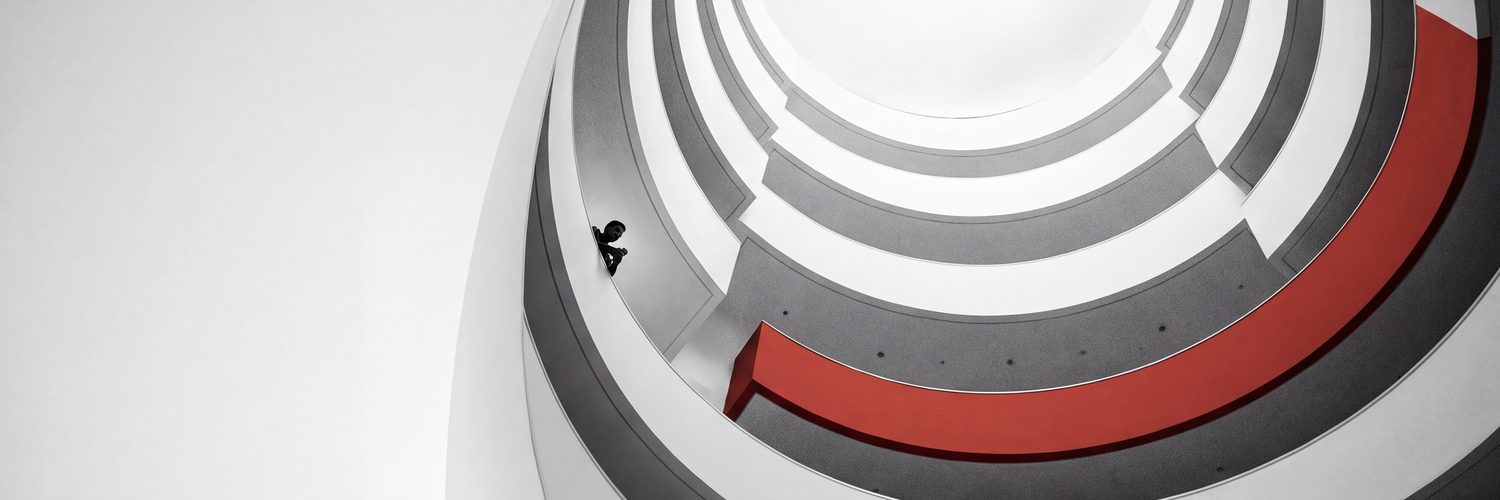 Looking up a white spiral atrium with one red balcony band and a lone figure at the rail